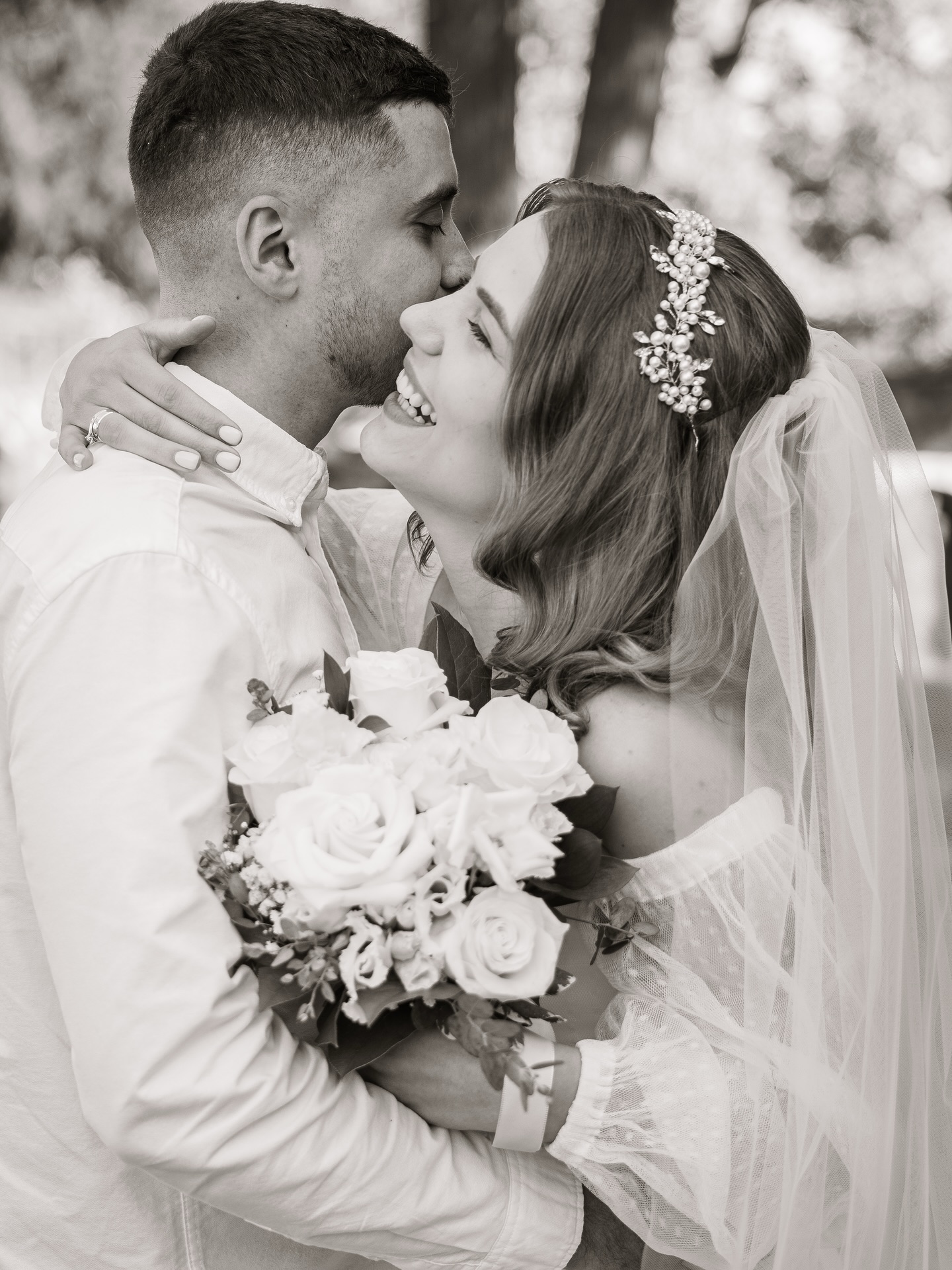 Black and white portrait of the groom kissing the laughing bride